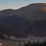 View of small, colorful wooden cottages scattered across the green mountain slopes of Bakhmaro village in Guria, Georgia. Landscape photo by Georgian artist Zurab Kostava.