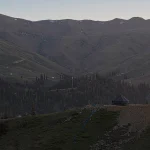 A distinctive wooden structure with a sharp, tent-like roof standing amidst the rolling green hills of Bakhmaro, Guria, Georgia. Architectural landscape photo by Georgian artist Zurab Kostava.