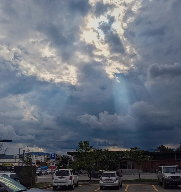 A dramatic sky with dark, heavy clouds and bright crepuscular rays (sunbeams) breaking through the center. Below, a foreground of a parking lot with cars and the low-profile building of a Wendy's restaurant.